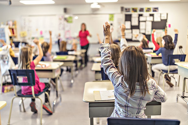 Barn håller upp ena handen i klassrumet